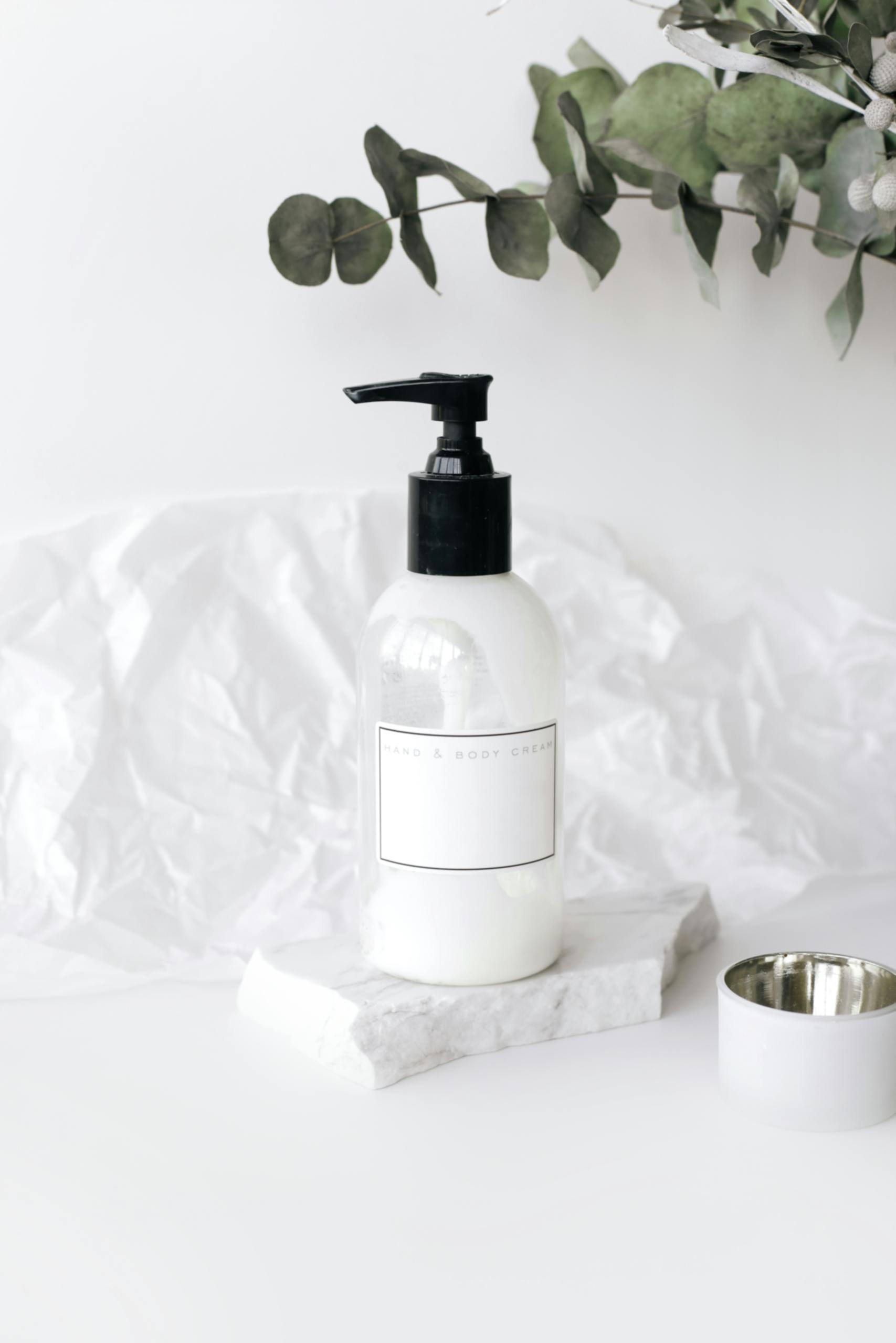 Elegant lotion bottle on marble with green leaves, perfect for skincare ads.