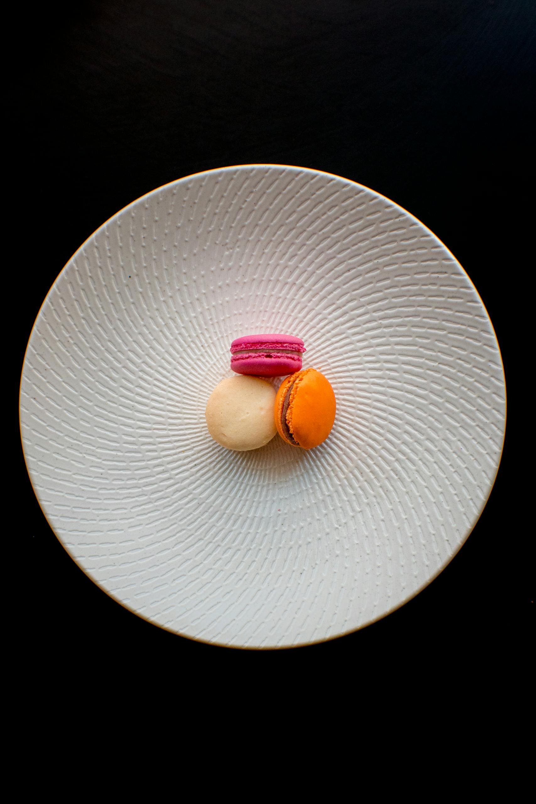Top-down view of colorful French macarons on a textured plate against a black background.