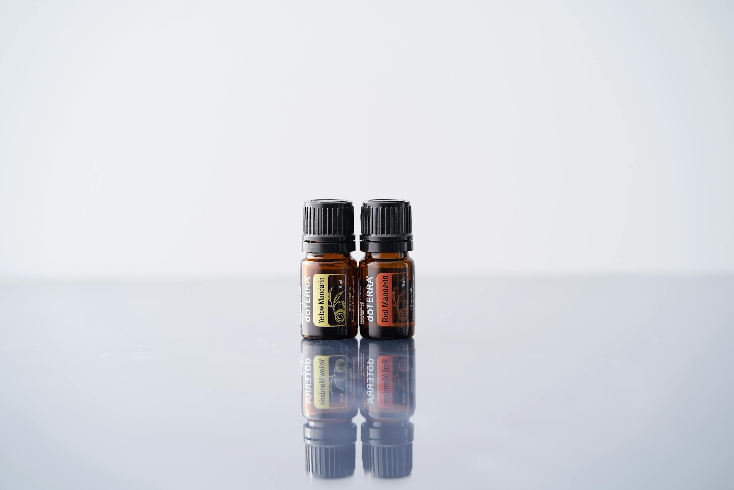 Two amber essential oil bottles sit on a reflective surface against a white background.